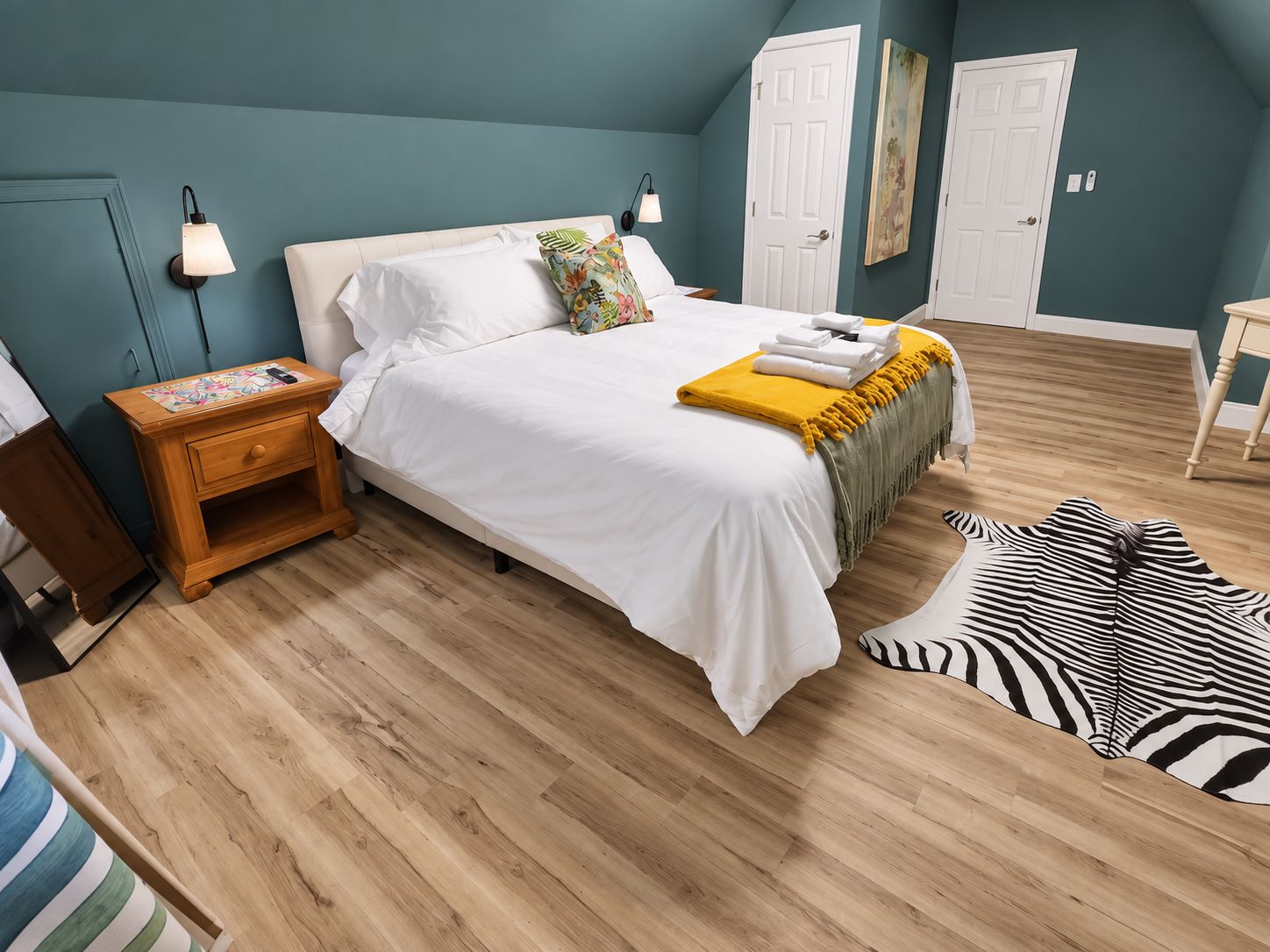 Un dormitorio con cama, mesitas de noche, una alfombra con estampado de cebra y una puerta.