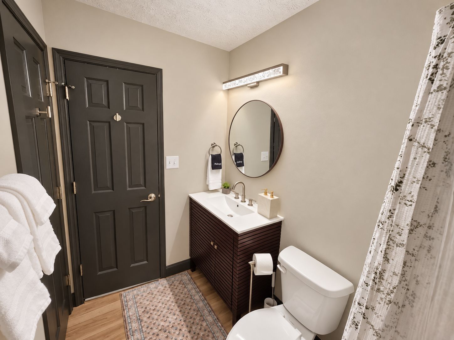 A bathroom with a dark door, a white sink, a mirror, a toilet, and a shower curtain.