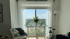 Ein Wohnzimmer mit Blick auf eine Brücke, ein blaues Sofa, ein Sessel mit gemustertem Kissen, ein kleiner Tisch mit Pflanzen und eine Stehlampe.