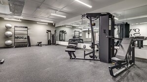 Ein Fitnessraum mit verschiedenen Trainingsgeräten, einer Spiegelwand und einem Hantelständer.