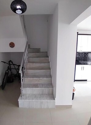 Una escalera con barandilla de metal, una bicicleta y una lámpara colgante.