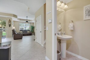 A spacious living room with a sofa, a dining area, and a bathroom with a sink and towel rack. - Relaxed Florida Living | Gated Community with Heated Pool | Near Beaches, Shopping & Dining (Fort Myers)