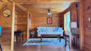 Interior de una cabaña de madera con un sofá, una mesa, un ventilador y un ventilador de techo.