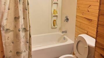 Et badeværelse med badekar, toilet og bruseforhæng.