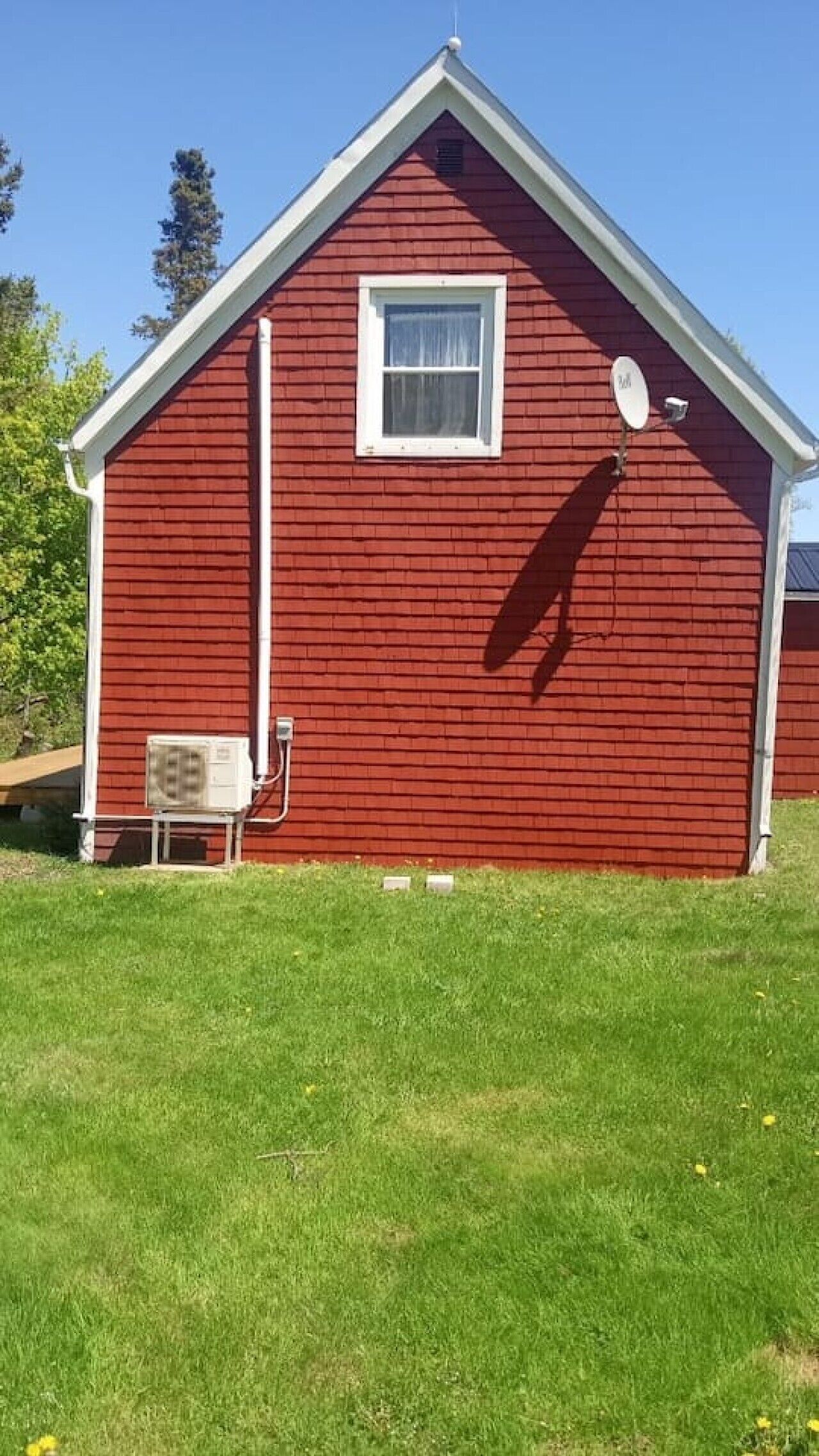 Un bâtiment en bois rouge avec une fenêtre blanche, une antenne parabolique et un climatiseur sur le côté.