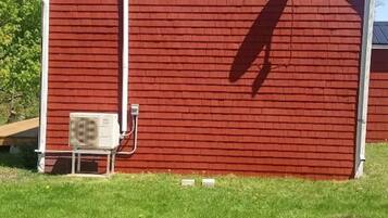 Un bâtiment en bois rouge avec une fenêtre blanche, une antenne parabolique et un climatiseur sur le côté.