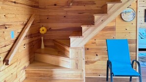 Un interior de madera con una escalera, una silla azul y un objeto circular montado en la pared.