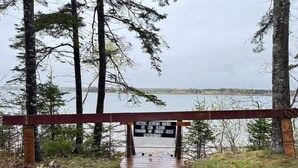 Una escalera de madera que baja a la orilla de un río, con un letrero de advertencia sobre el peligro de la escalera.