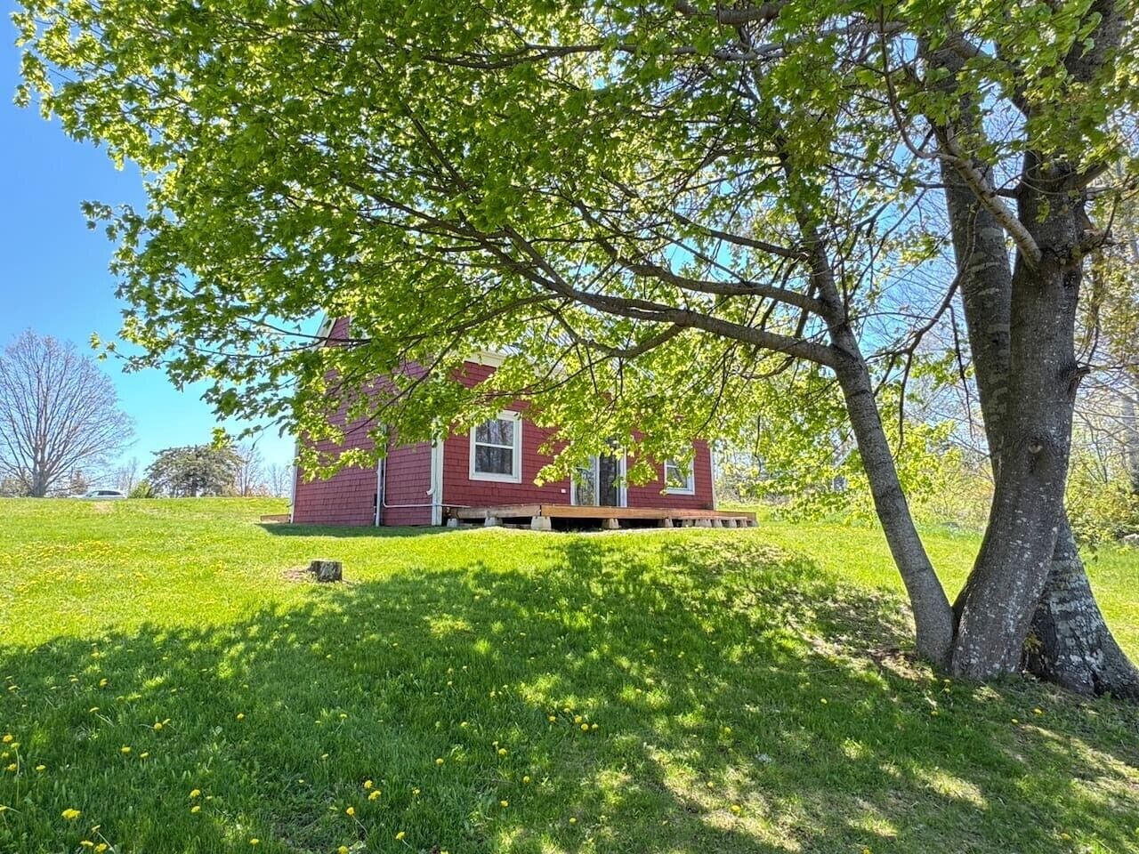 A red house with a porch, surrounded by a grassy yard and trees.