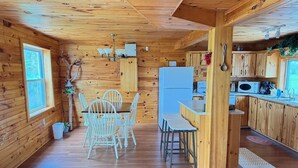 Interior de una cabaña de madera con comedor, cocina y ventana.