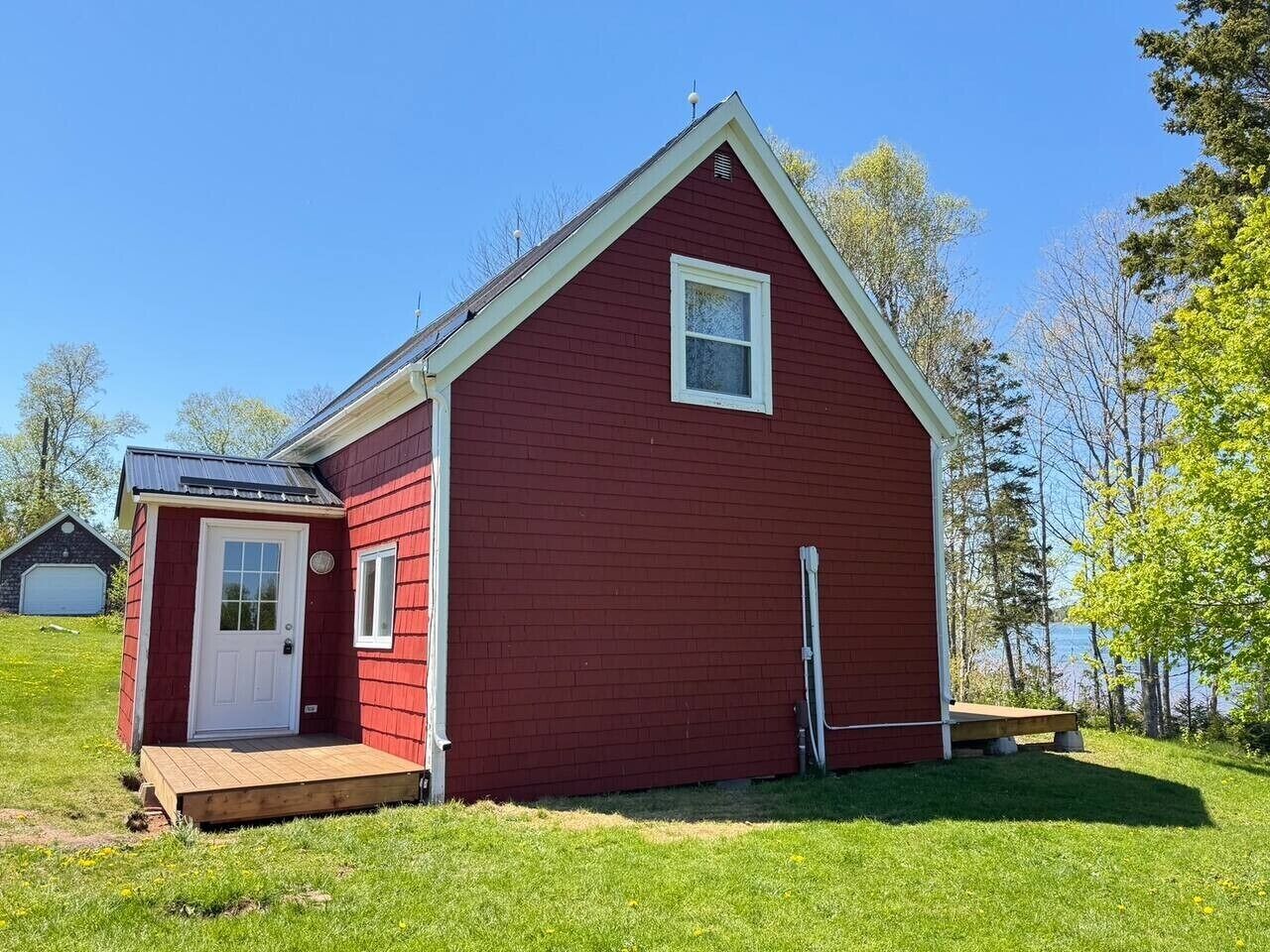 A red single-story house with a front porch, a small attached garage, and a clear view of the surrounding landscape.