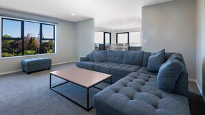 Un salon moderne avec un canapé d’angle, un pouf et une table basse.