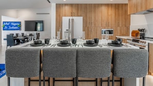 Une cuisine moderne avec des meubles en bois, un four encastré et un coin repas doté de chaises à revêtement gris.