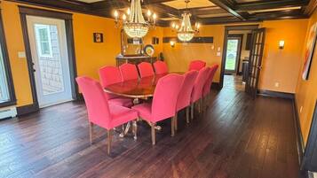 A dining area with a wooden table and red chairs, chandeliers, and a view through a glass door.