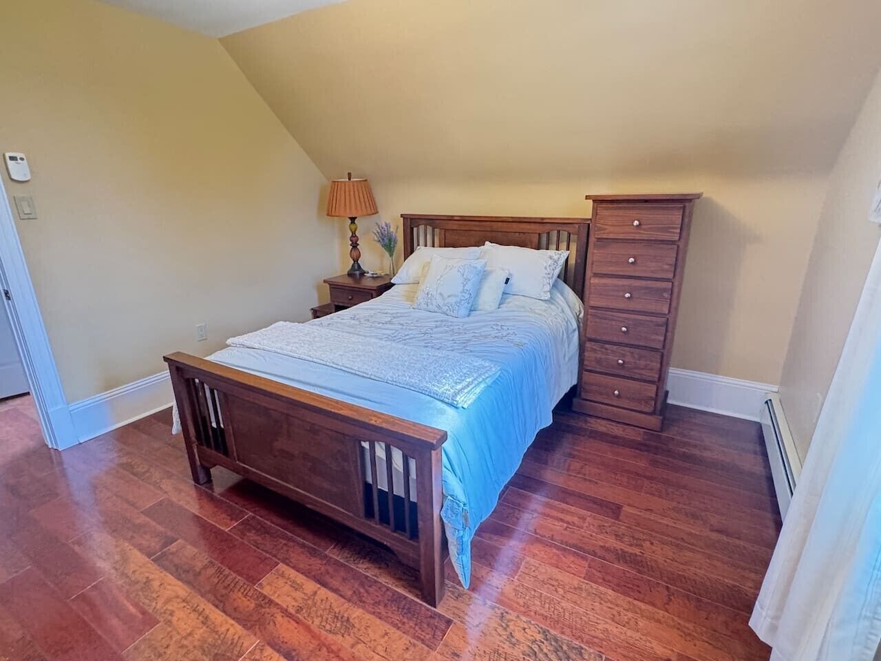 A bedroom with a wooden bed, a nightstand, a dresser, and a lamp.
