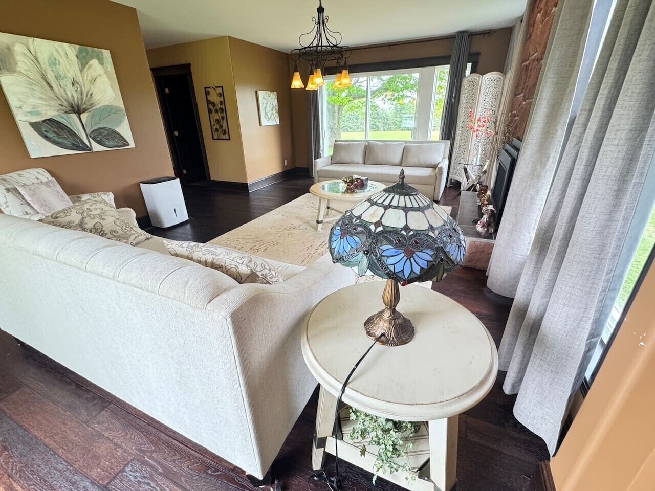 A living room with a sofa, a round table with a lamp, and a view of the outdoors.