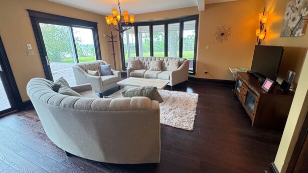 A living room with dark wood flooring, a large window, and a chandelier. - Cedayway Riverview Estate-by Brudenell River overseeing golf course (Montague)