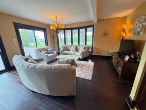 Un salon doté d’un parquet en bois foncé, d’une grande fenêtre et d’un lustre.