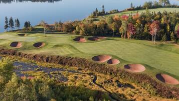 Un campo da golf con bunker, un lago e alberi con foglie autunnali.