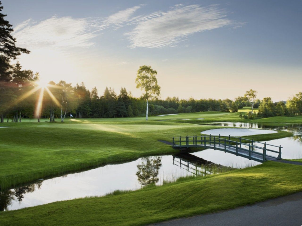 A golf course with a pond, a bridge, and a flag.