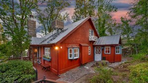Et rødt træhus med en stenbelagt veranda, skorsten og et mindre tilbygget hus.