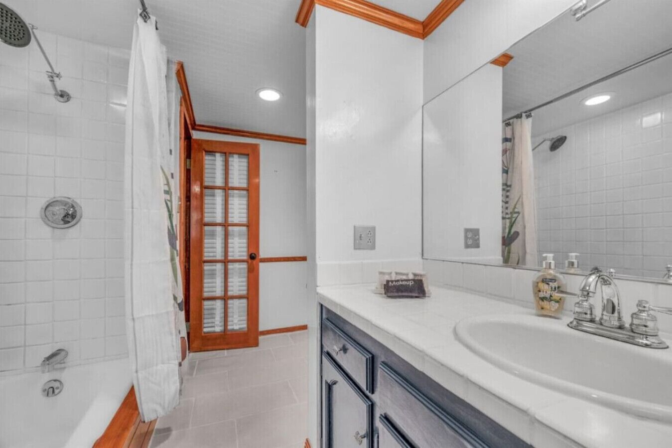 A bathroom with a shower, a sink, a mirror, and a door leading to another room.
