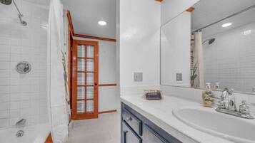 A bathroom with a shower, a sink, a mirror, and a door leading to another room.