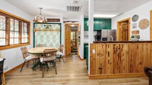 A dining area with a round table and chairs, a kitchen with green cabinets, and a breakfast sign. - River Falls - Hot Tub and Mountain Views sleeps 4 (Oakhurst)
