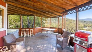 A covered outdoor patio with wooden flooring, a grill, wicker furniture, and a hot tub. - River Falls - Hot Tub and Mountain Views sleeps 4 (Oakhurst)
