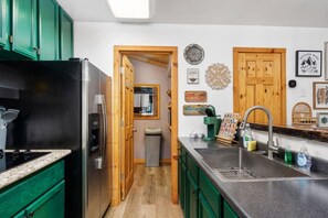 Une cuisine avec des meubles de couleur verte, un évier en acier inoxydable et un réfrigérateur.