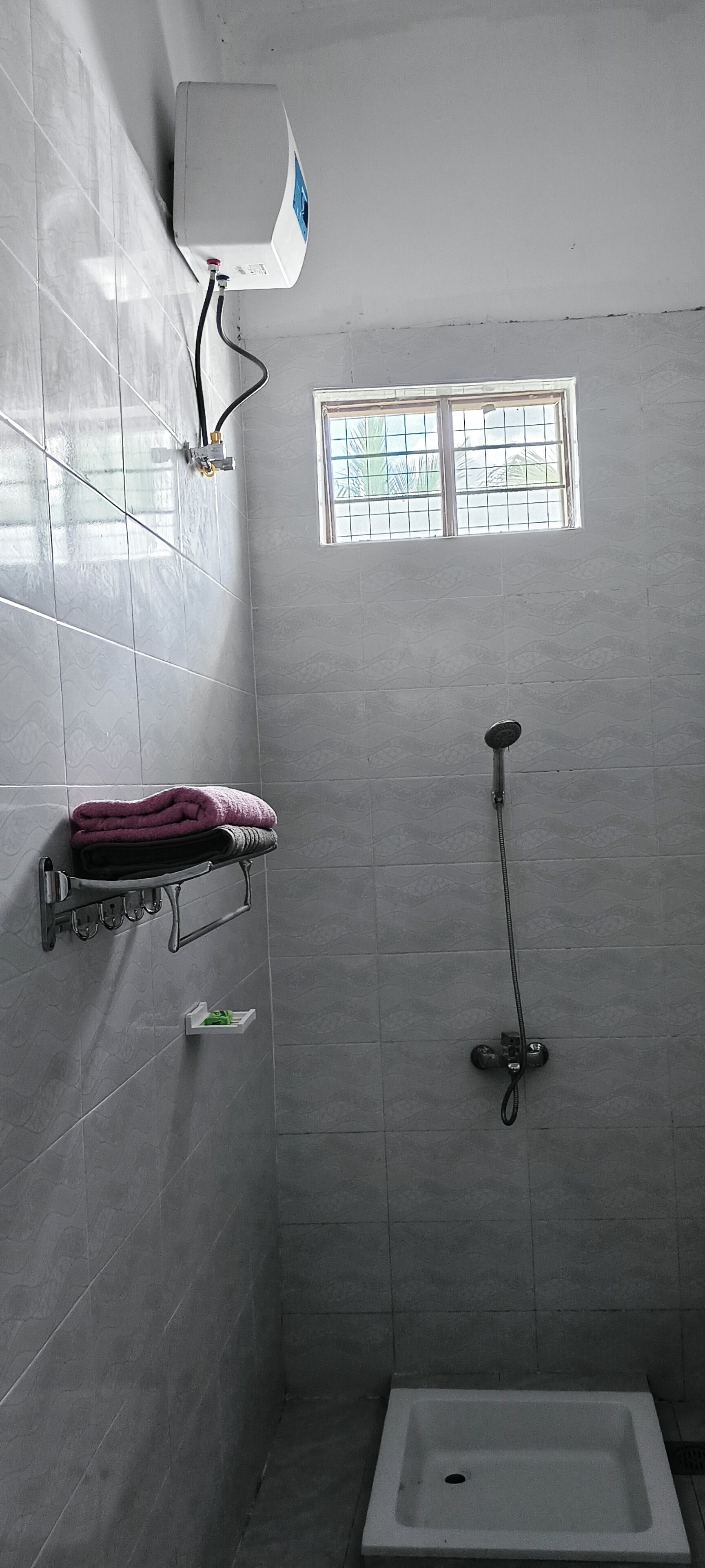 A bathroom with a shower, a towel rack, a window, and a toilet.