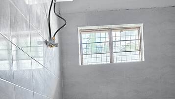 A bathroom with a shower, a towel rack, a window, and a toilet.