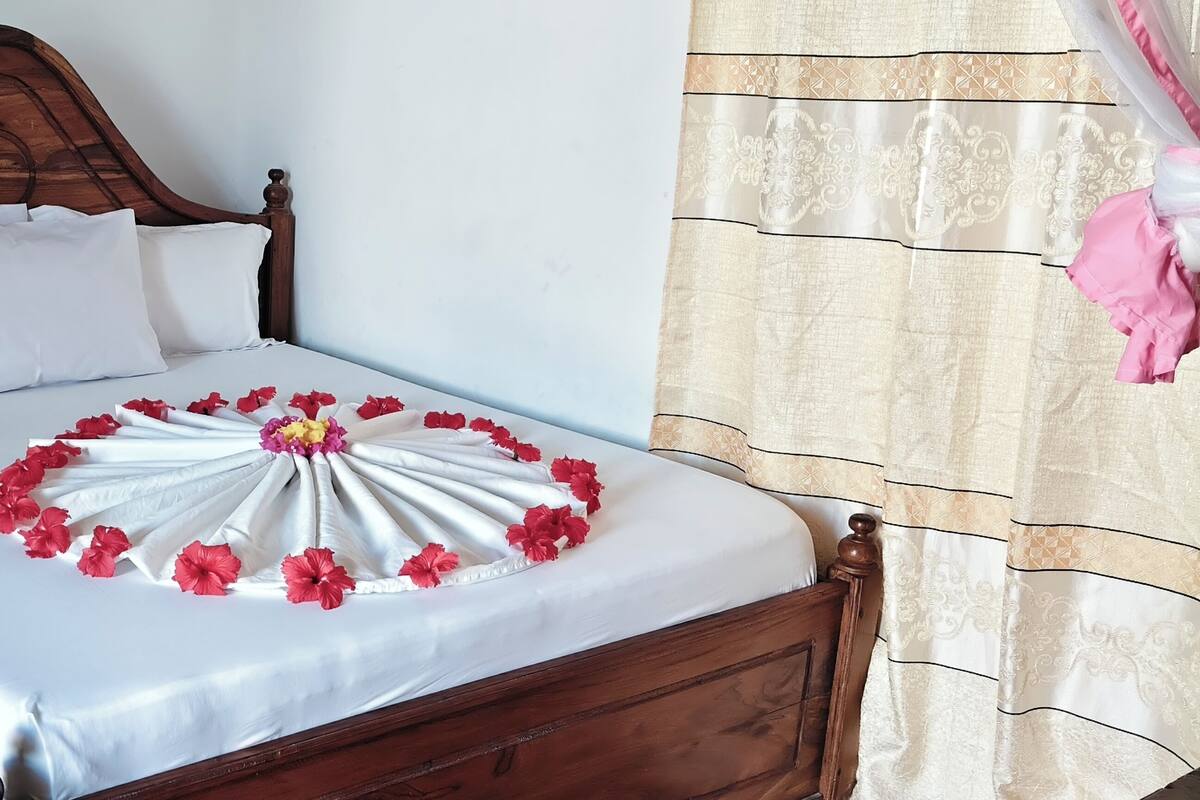 A bed with a white sheet, a wooden headboard, and a decorative arrangement of white and red flowers on the bedspread.