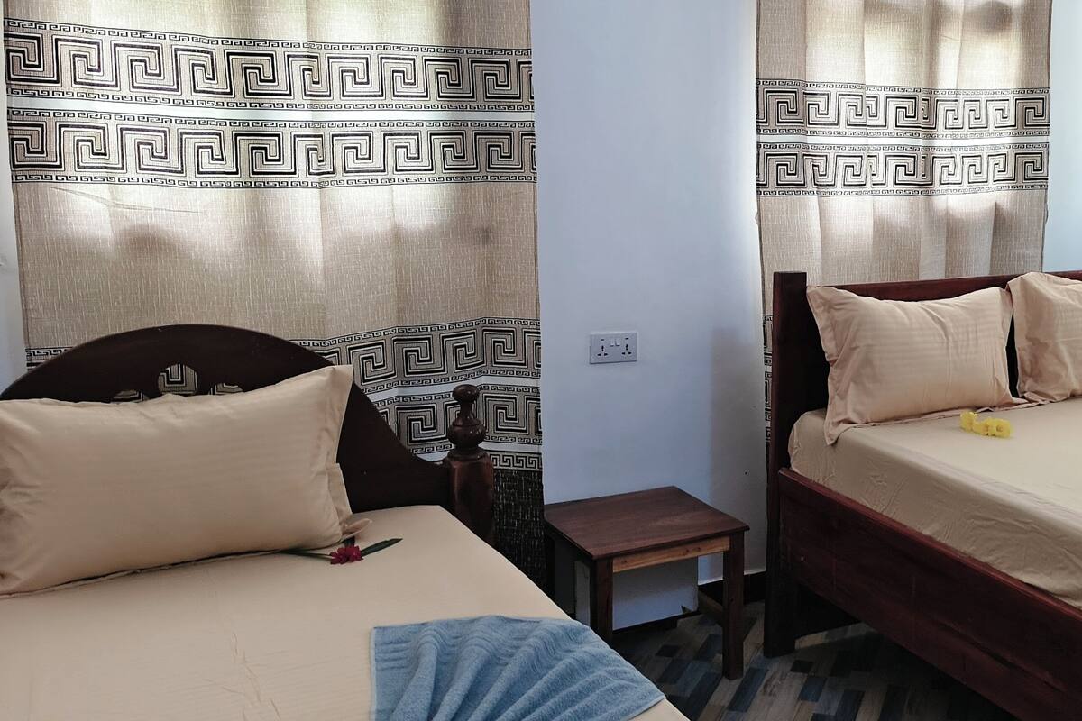A room with two beds, a small table, and curtains with a geometric pattern.