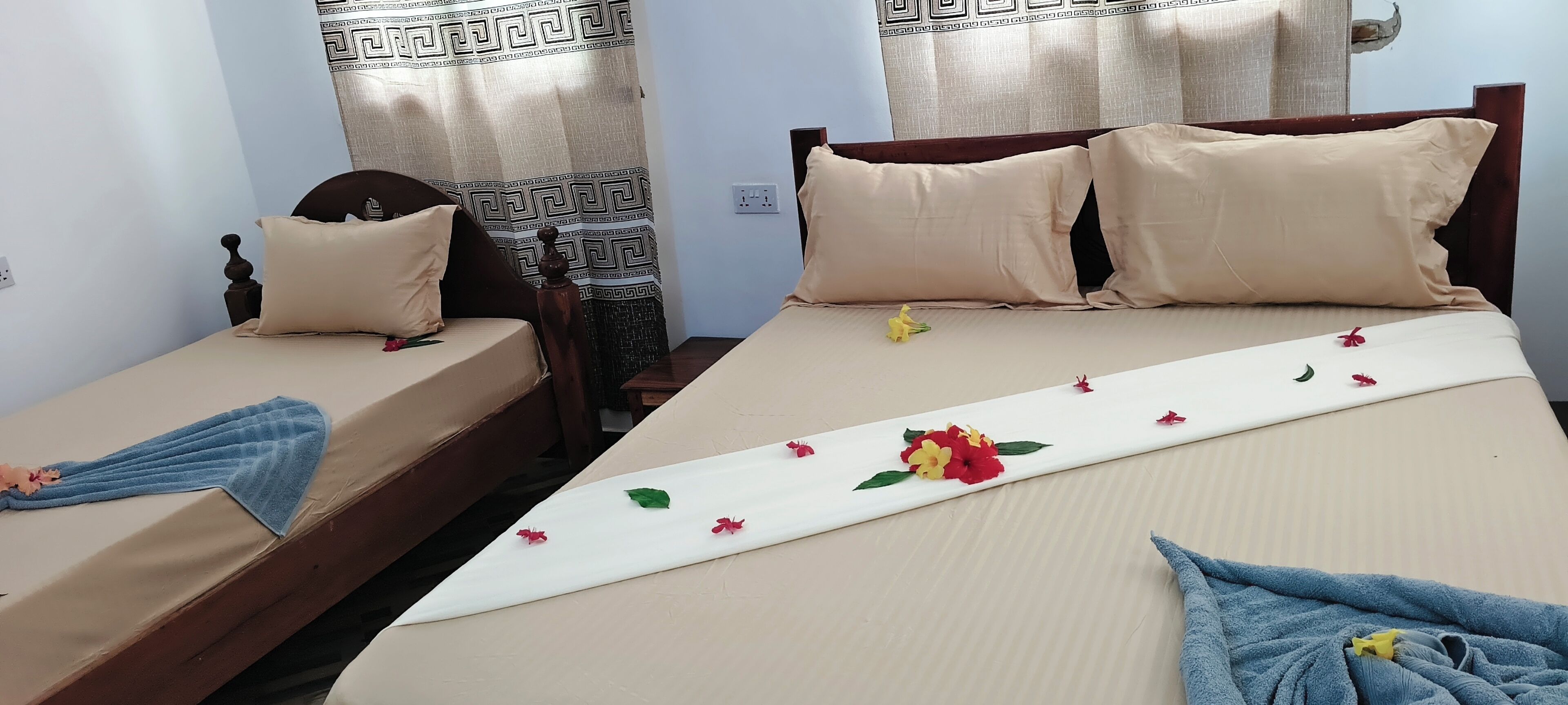 Two single beds with wooden frames, beige bedding, and a decorative floral arrangement on the larger bed.