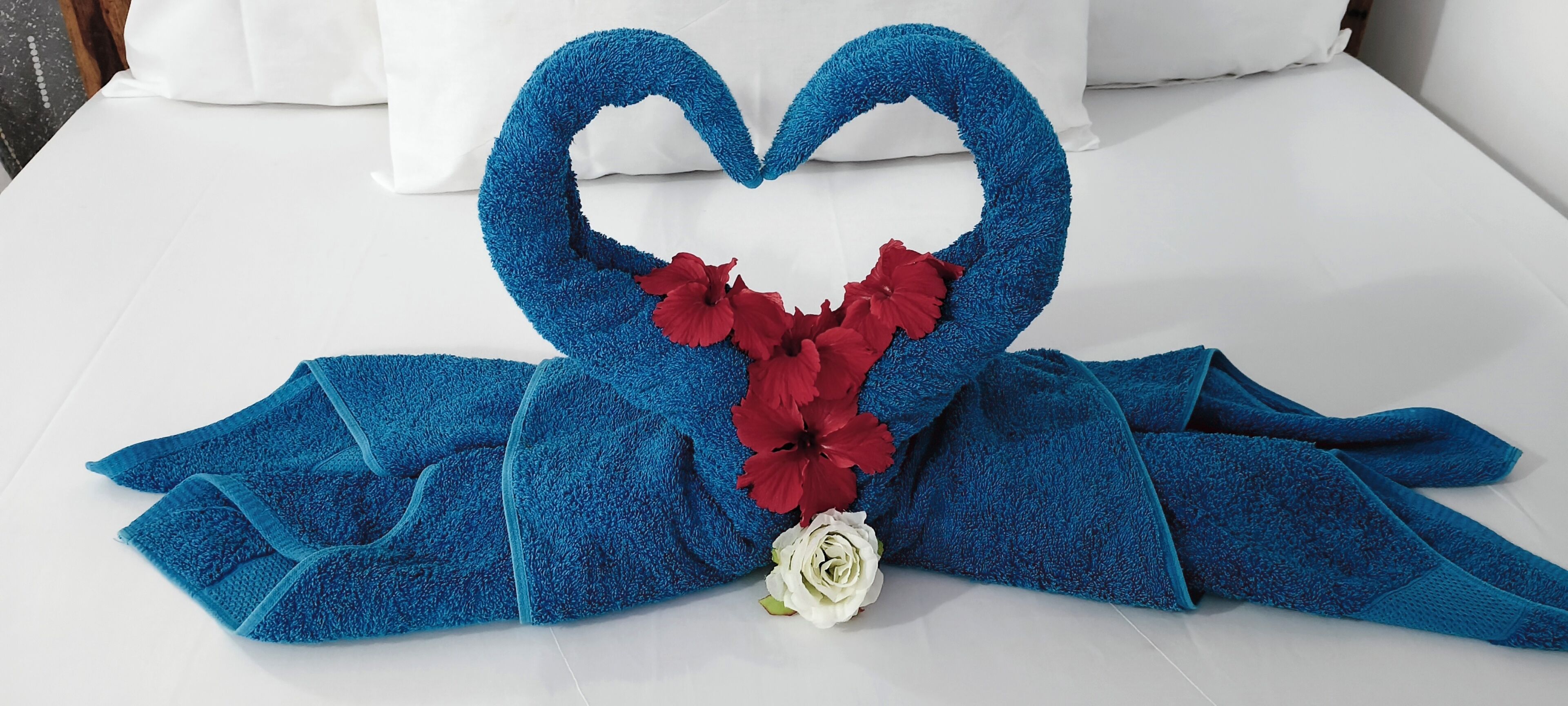 Un lit décoré de serviettes pliées en forme de cœur et de fleurs.
