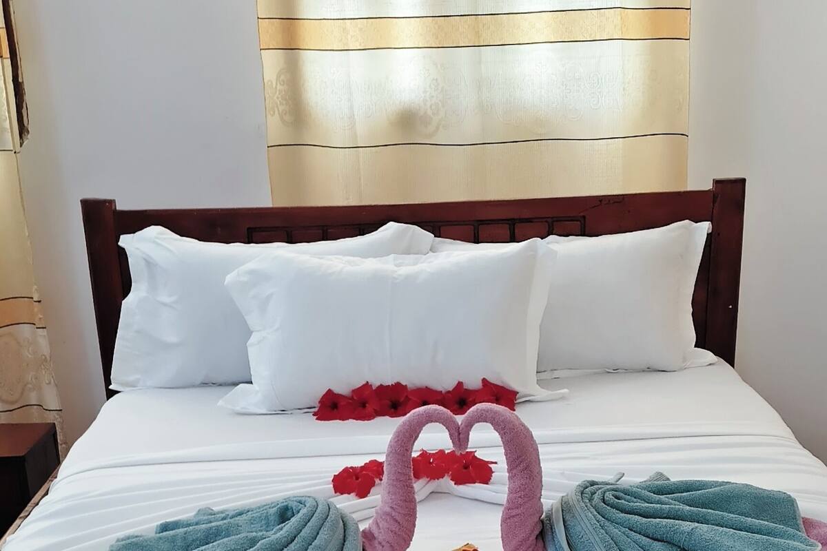 A neatly made bed with white linens, two towels arranged in a heart shape, and a wooden headboard.