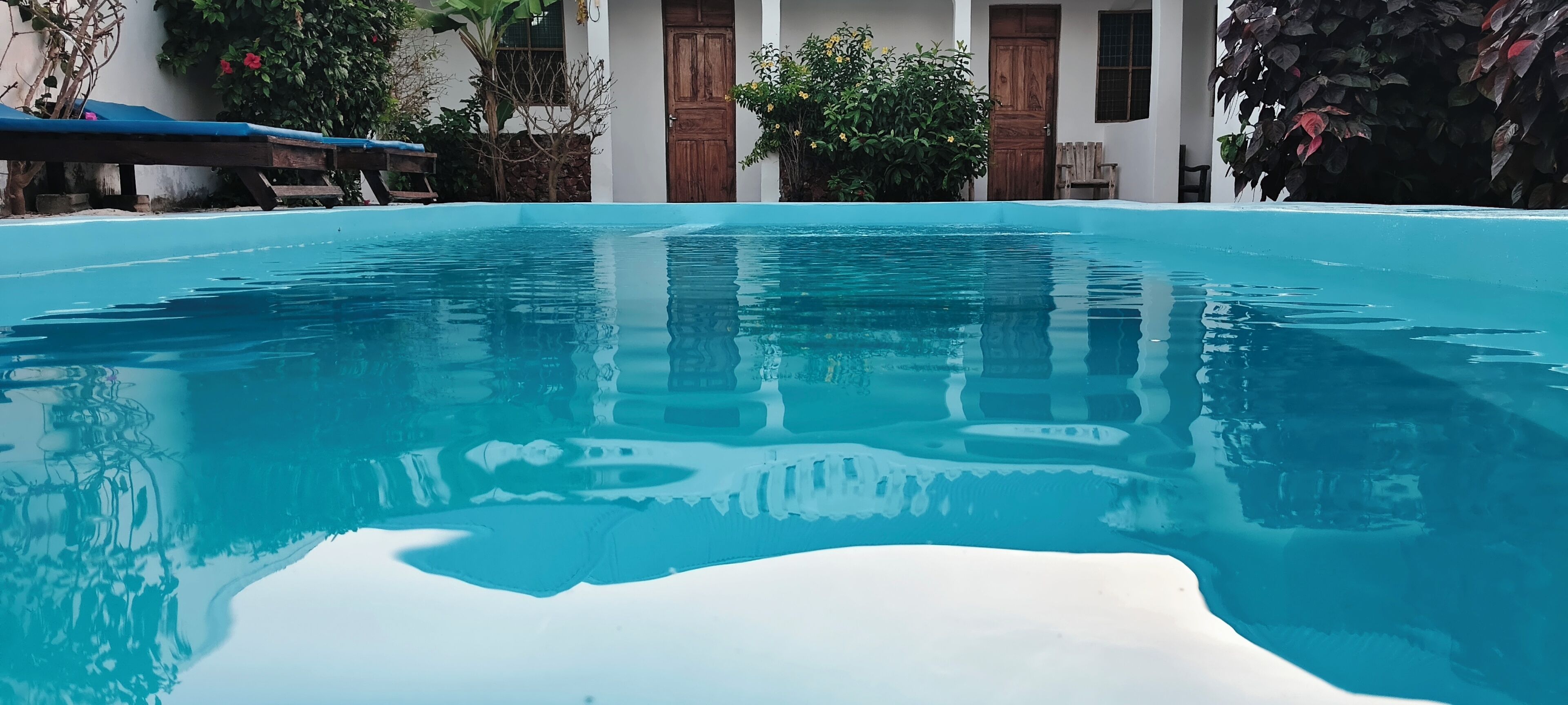 Piscina cristalina con reflejos, rodeada por un edificio de puertas de madera y plantas.