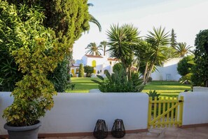 A courtyard with a white building, palm trees, and a yellow gate. - Algarve escape in the heart of the prestigious Golden Triangle (Quarteira)