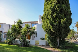 A white building with a yellow door, surrounded by greenery and a tall tree. - Algarve escape in the heart of the prestigious Golden Triangle (Quarteira)