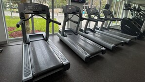 Une salle de sport équipée de tapis de course, d’un écran de télévision et de grandes fenêtres donnant sur un espace vert.