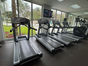 A gym with treadmills, a TV screen, and large windows overlooking a green area. - Bright 1 Bedroom Near Beach & Shops (Sunny Isles Beach)