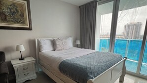 Une chambre à coucher avec un lit, une table de chevet, une lampe, un tableau et une vue sur une piscine.