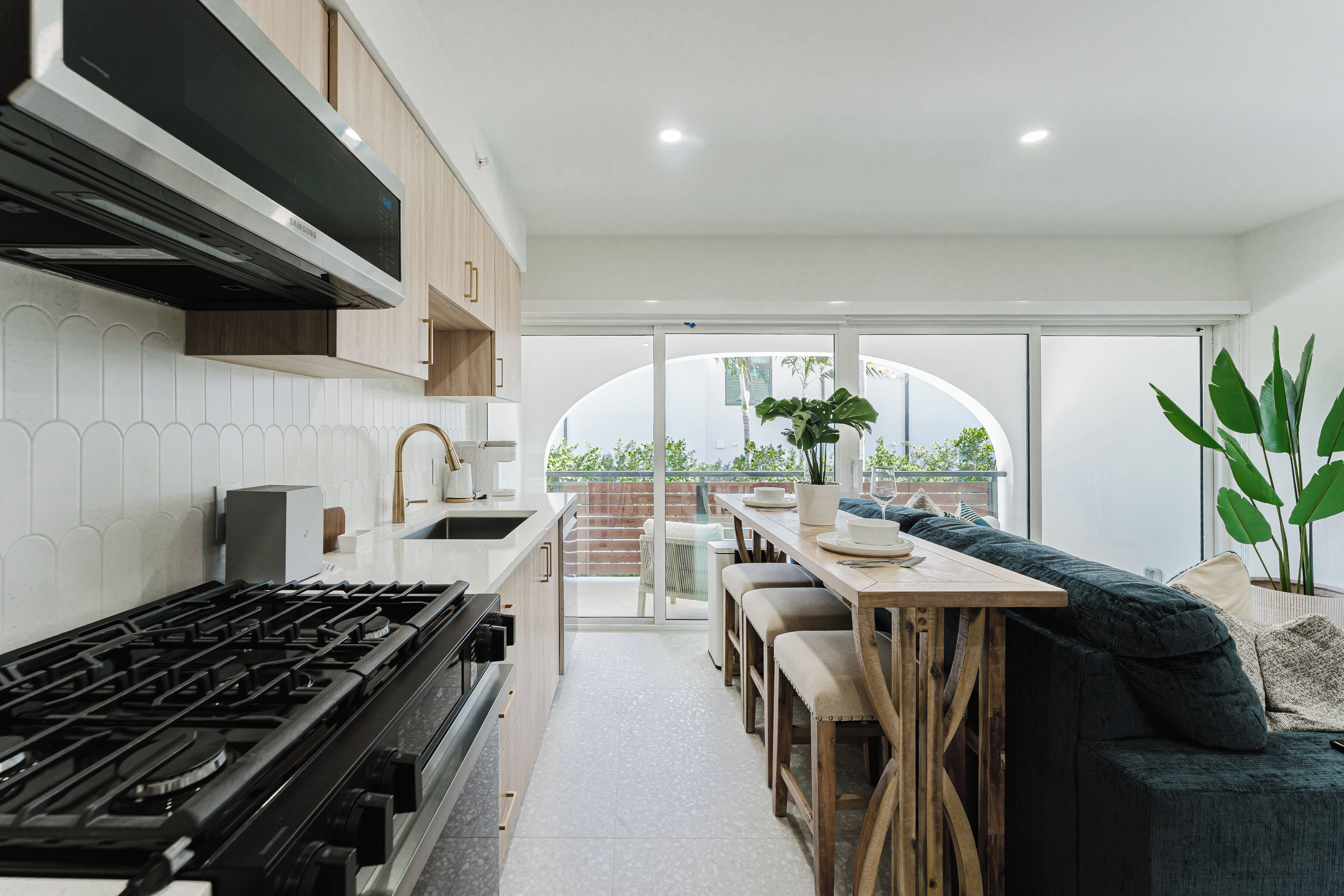A modern kitchen with a gas stove, wooden cabinets, and a dining area with a sofa and table.