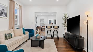 A modern living room with a sofa, a coffee table, a TV, and a dining area in the background.