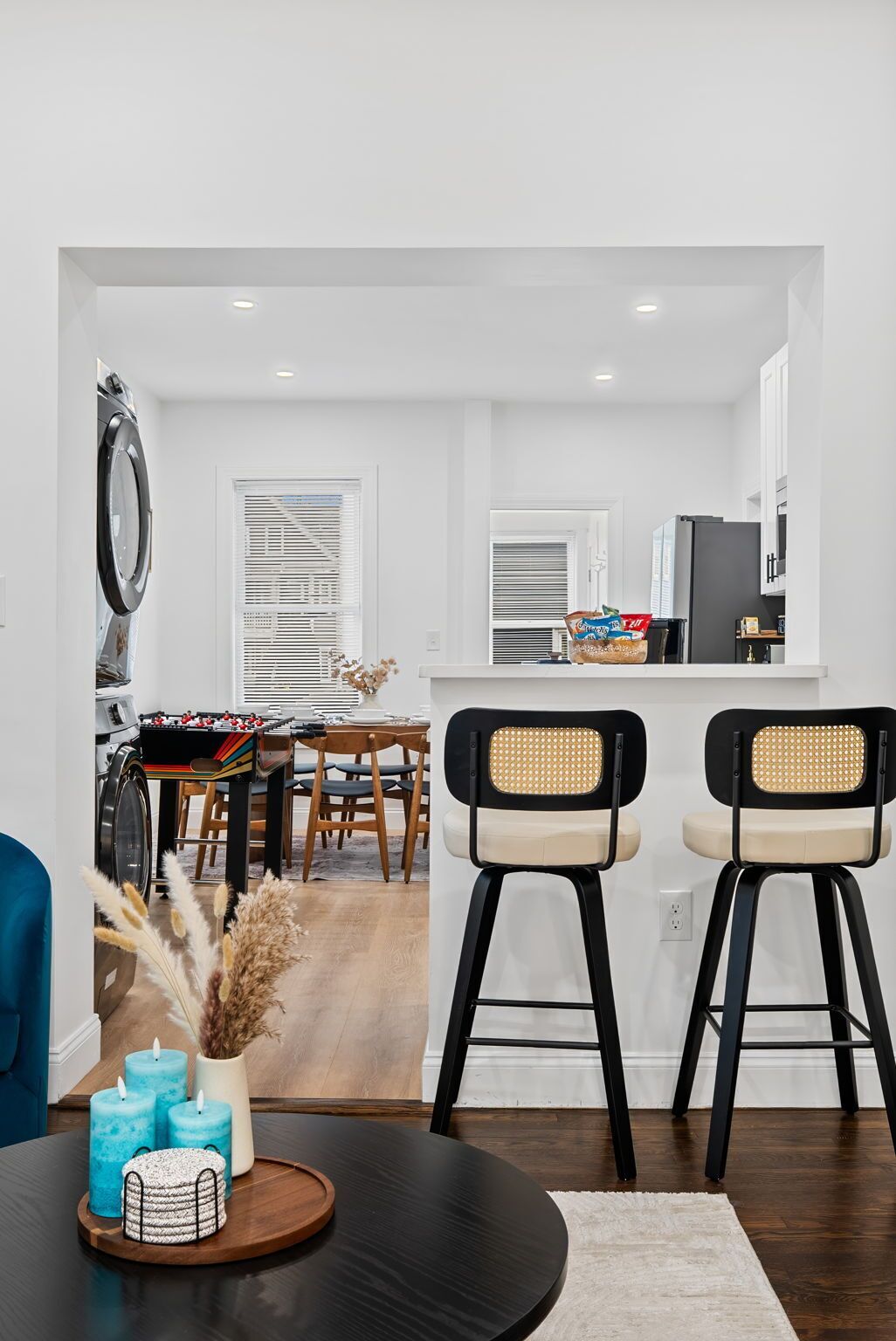 Une cuisine moderne avec un coin repas, deux tabourets de bar, une table ronde décorée de bougies et un lave-linge visible.