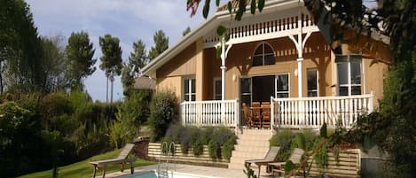 A two-story house with a pool, outdoor furniture, and a garden.