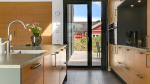 A modern kitchen with a large island, stainless steel appliances, and a sliding glass door leading to an outdoor area. - "Uschi" - 1km from the sea by Interhome (Blokhus)