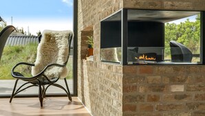 A modern room with a brick wall, a glass fireplace, a furry chair, and a view of greenery. - "Uschi" - 1km from the sea by Interhome (Blokhus)
