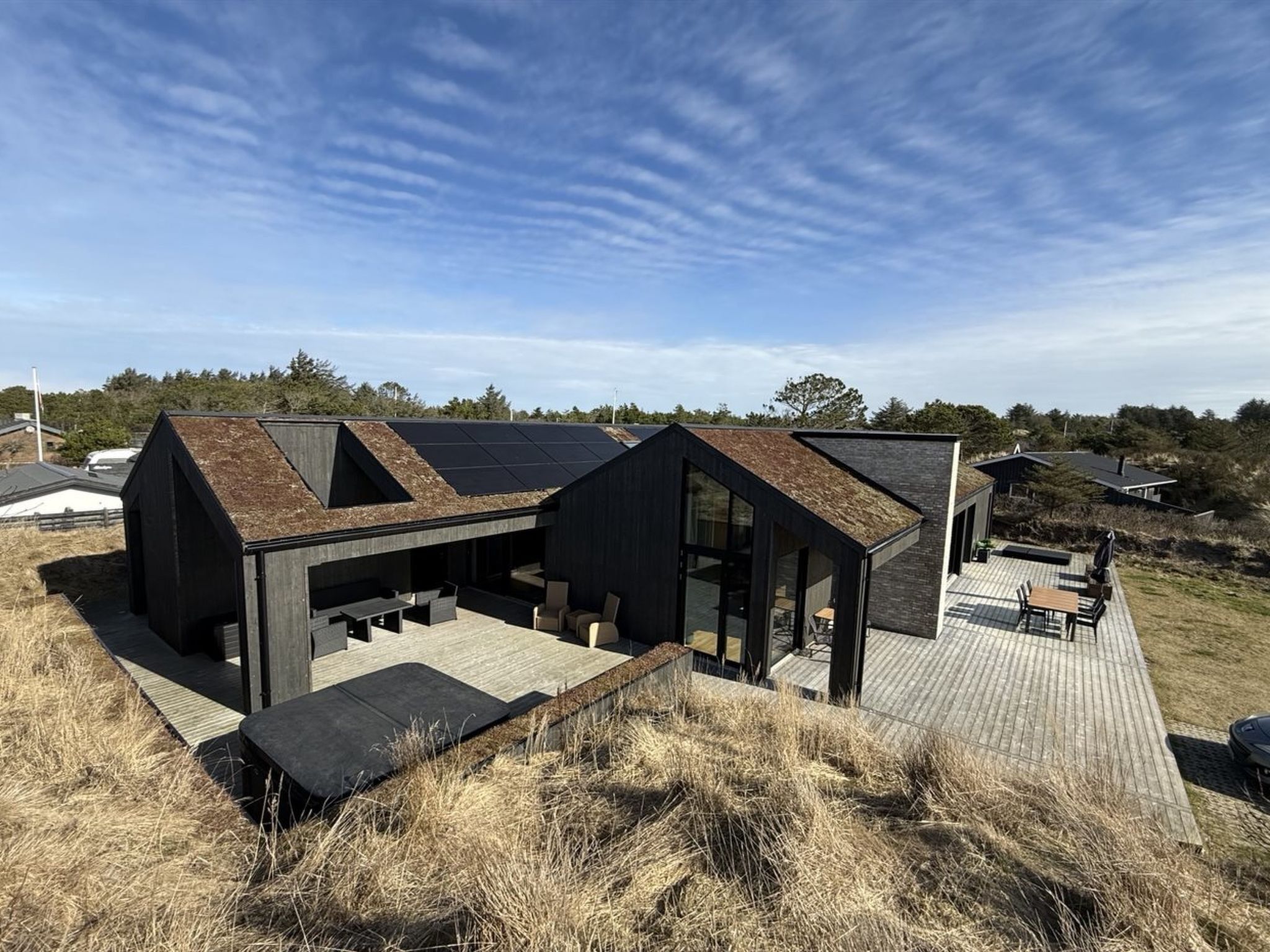Ein modernes Haus mit einer großen Terrasse, Solaranlage und einem geneigten Dach.